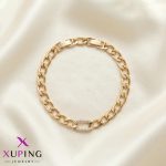 دستبند زنجیری طلایی رنگ برند ژوپینگ (Xuping) با یک حلقه بیضی شکل پر از نگین‌های ریز در وسط، که به شکل دایره روی پارچه ساتن روشن قرار گرفته است.