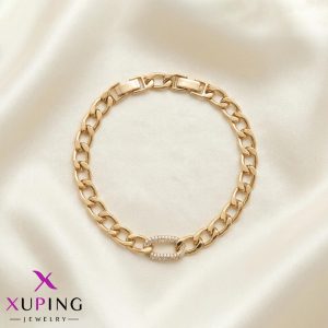 دستبند زنجیری طلایی رنگ برند ژوپینگ (Xuping) با یک حلقه بیضی شکل پر از نگین‌های ریز در وسط، که به شکل دایره روی پارچه ساتن روشن قرار گرفته است.