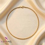 زنجیر طنابی طلایی رنگ برند ژوپینگ (Xuping) که روی یک پارچه حریر روشن قرار گرفته است.
