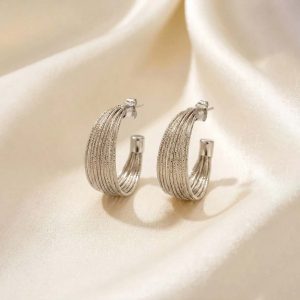 یک جفت گوشواره حلقه‌ای پهن و تراش خورده(بافت‌دار) نقره ای رنگ که روی پارچه حریر روشن قرار گرفته است