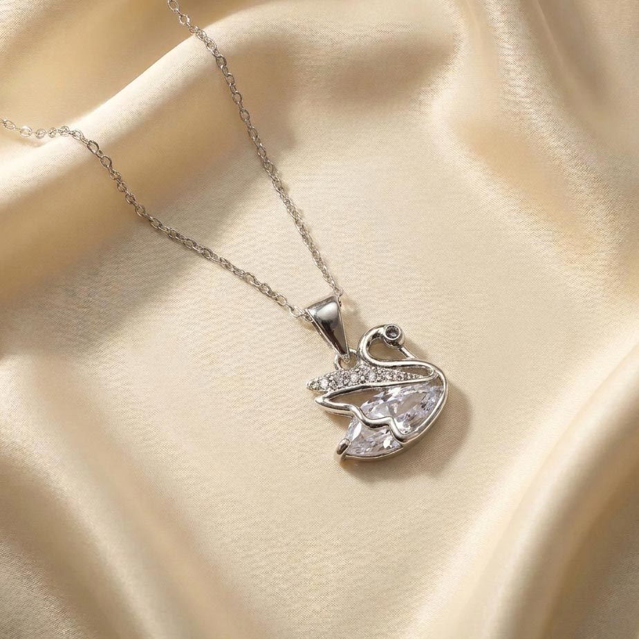 womens-silver-swan-crystal-necklace گردنبند نقرهای رنگ با پلاک طرح قو که بدن آن از یک کریستال بزرگ شفاف و قسمت بال و گردن آن با نگینهای ریز تزئین شده است روی پارچه ساتن کرم که زیبایی گردنبند طرح قو نقرهای را نشان میدهد.